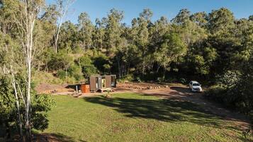 A campsite with a small wooden cabin, a paved area, and a dirt path leading to a vehicle.