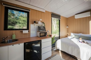 A modern bedroom with a bed, bedside table, and a view of the outdoors.