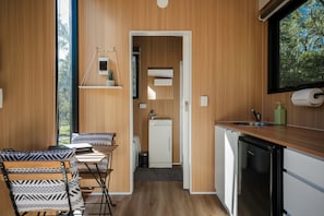 Cocina compacta con lavamanos, lavavajillas y ventana con vistas a un bosque.