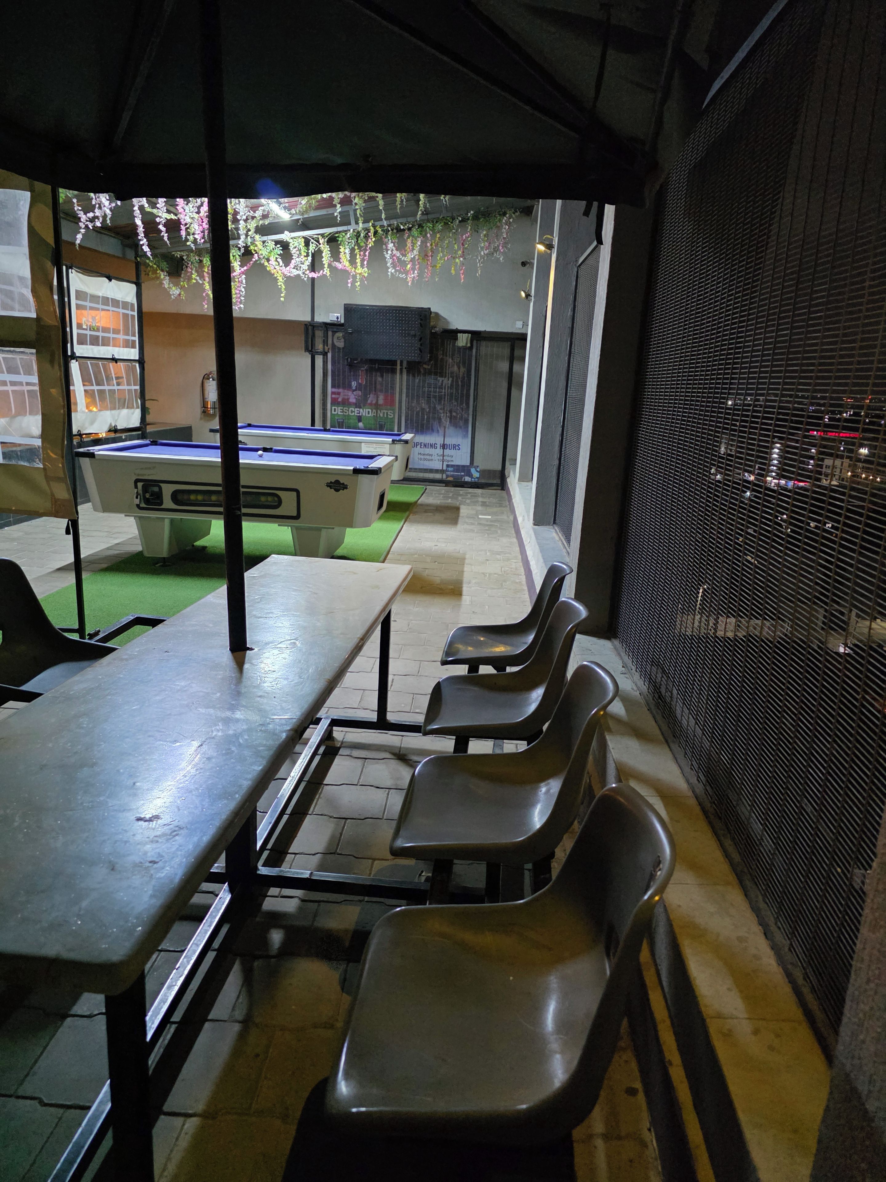 A billiards table under a covered area with chairs and a pool table visible in the background.