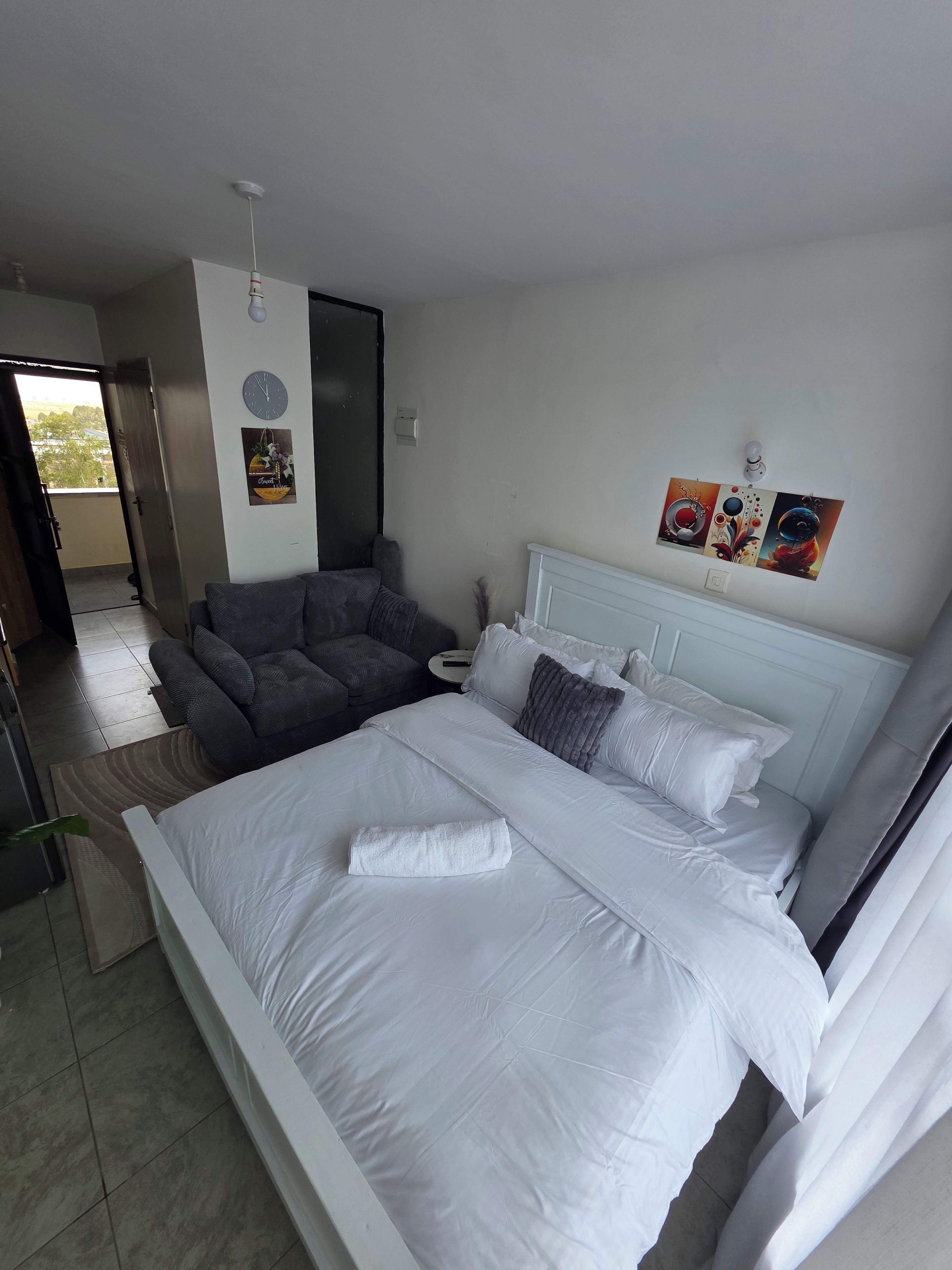 A hotel room with a bed, a sofa, a wall clock, and a painting.
