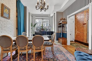 Un coin repas comprenant une table, des chaises et un lustre. De grandes fenêtres offrent une vue sur la ville.