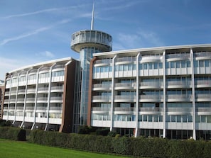 Ein mehrstöckiges Hotel mit einem zentralen Turm, Balkonen und einem gepflegten Rasen.