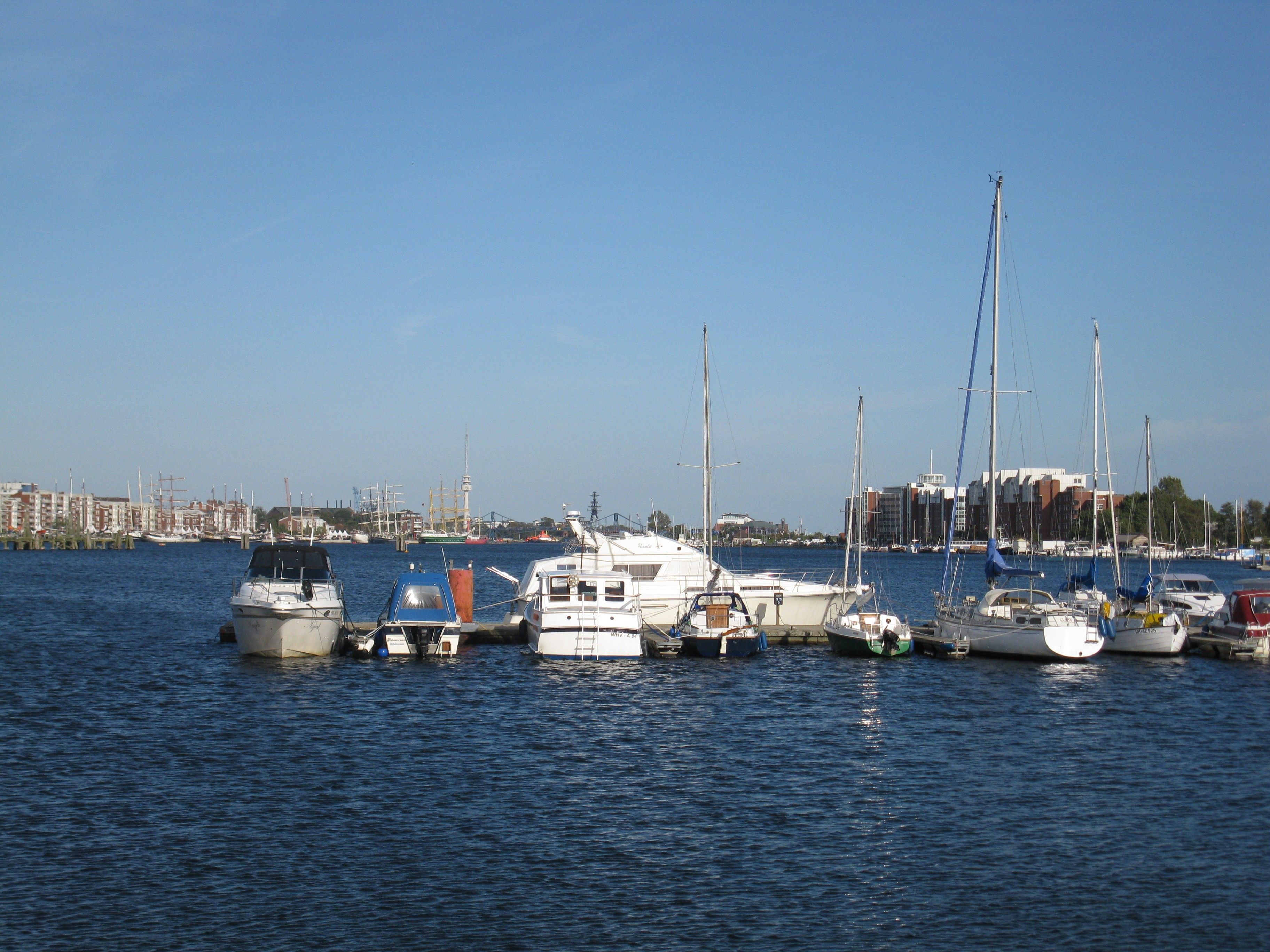 Een jachthaven met diverse boten afgemeerd, een heldere lucht en gebouwen op de achtergrond.