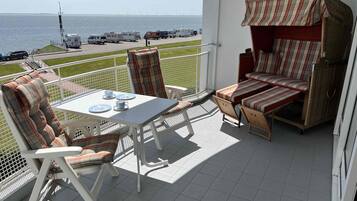 Ein Balkon mit Tisch und Stühlen, einem Korbsessel und Blick auf das Meer und Windkraftanlagen.