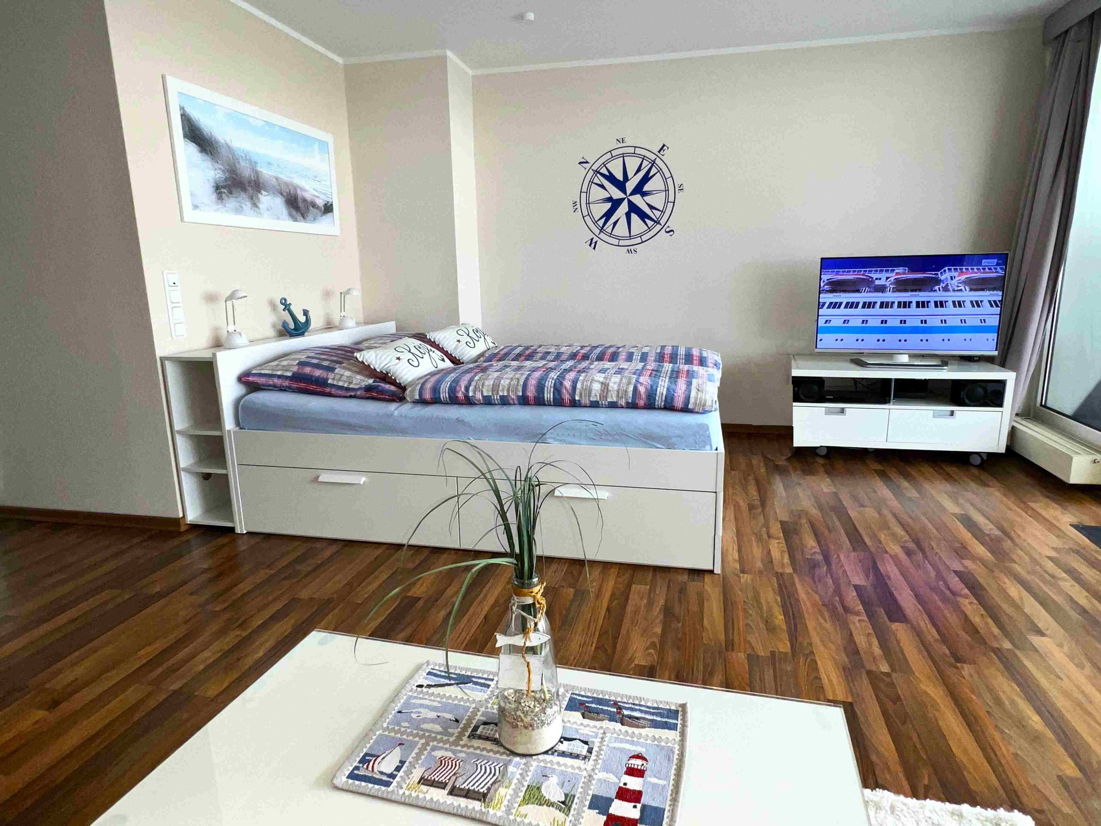 Ein Schlafzimmer mit einem Bett, einem Fernseher, einem Wandkompass und einem Fenster.