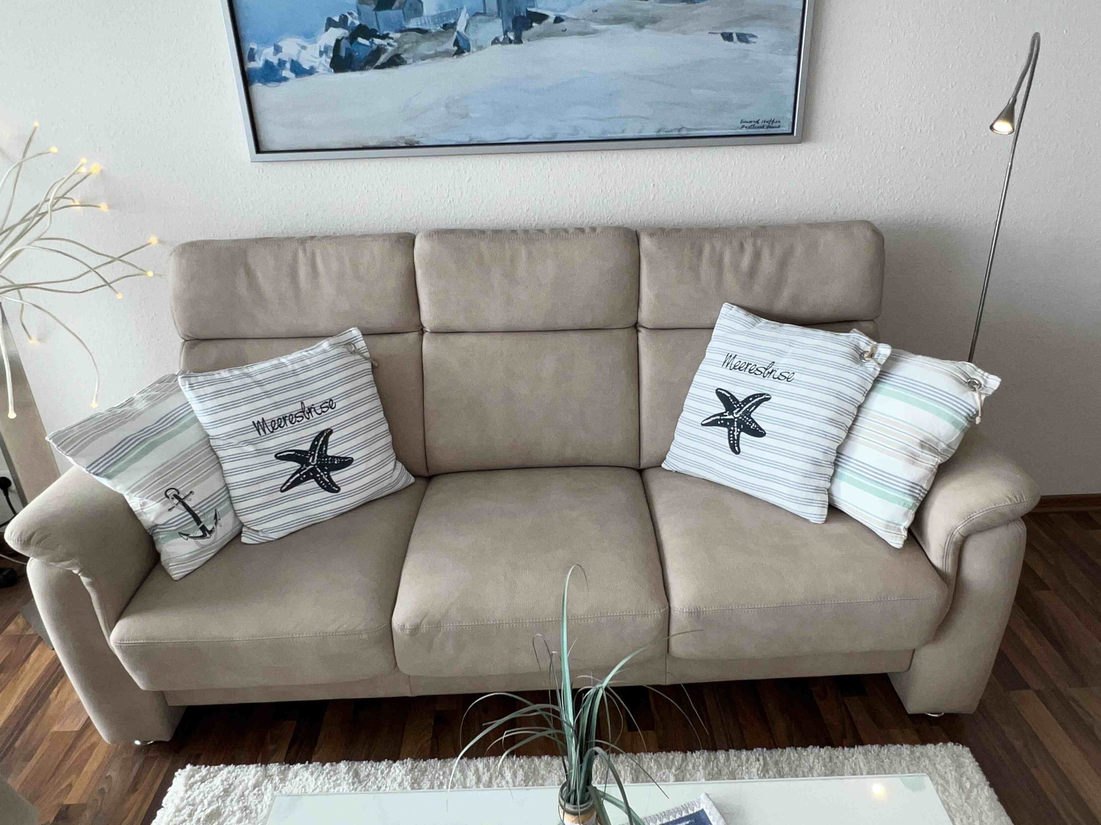 Un sofá color beige con dos almohadones, uno con un diseño de estrella de mar y el otro con la palabra 'Meereslust'.
