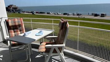 A balcony with a table and chairs, overlooking a parking area and the sea.