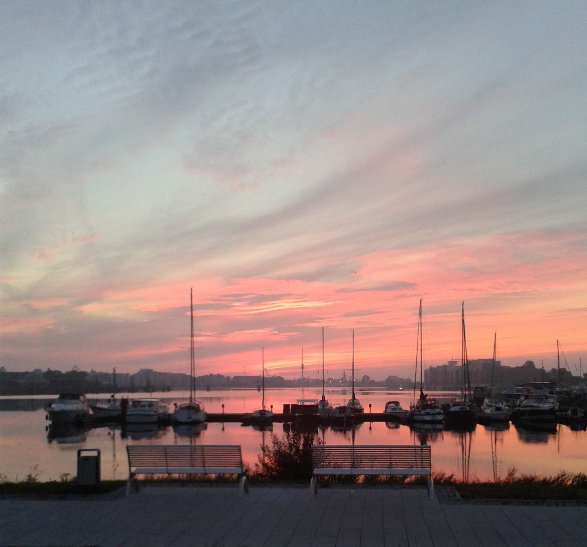 A marina with boats docked, a bench, and a calm water body reflecting the sky.