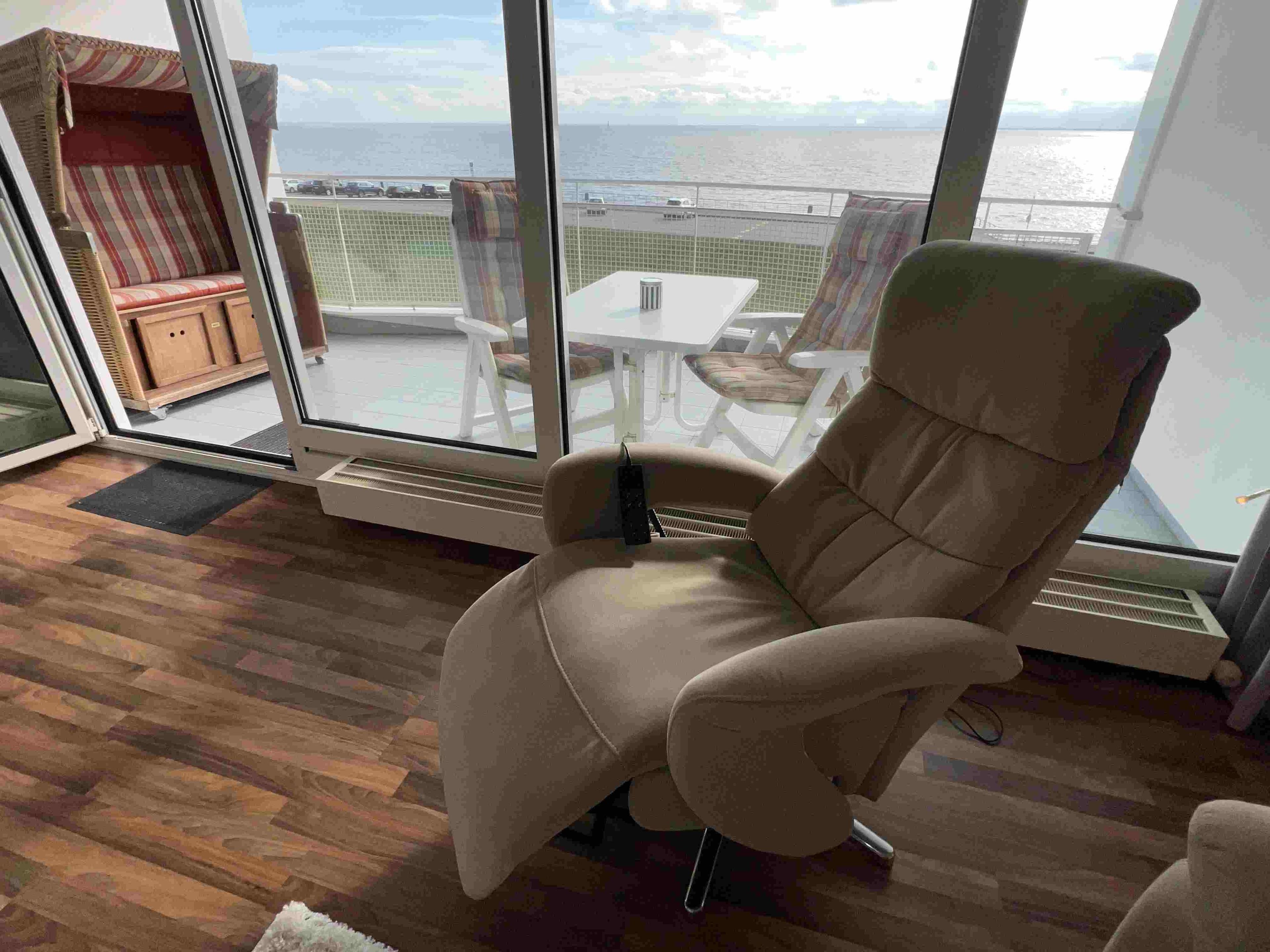 Een kamer met een groot raam, een fauteuil, een klein tafeltje en uitzicht op zee.