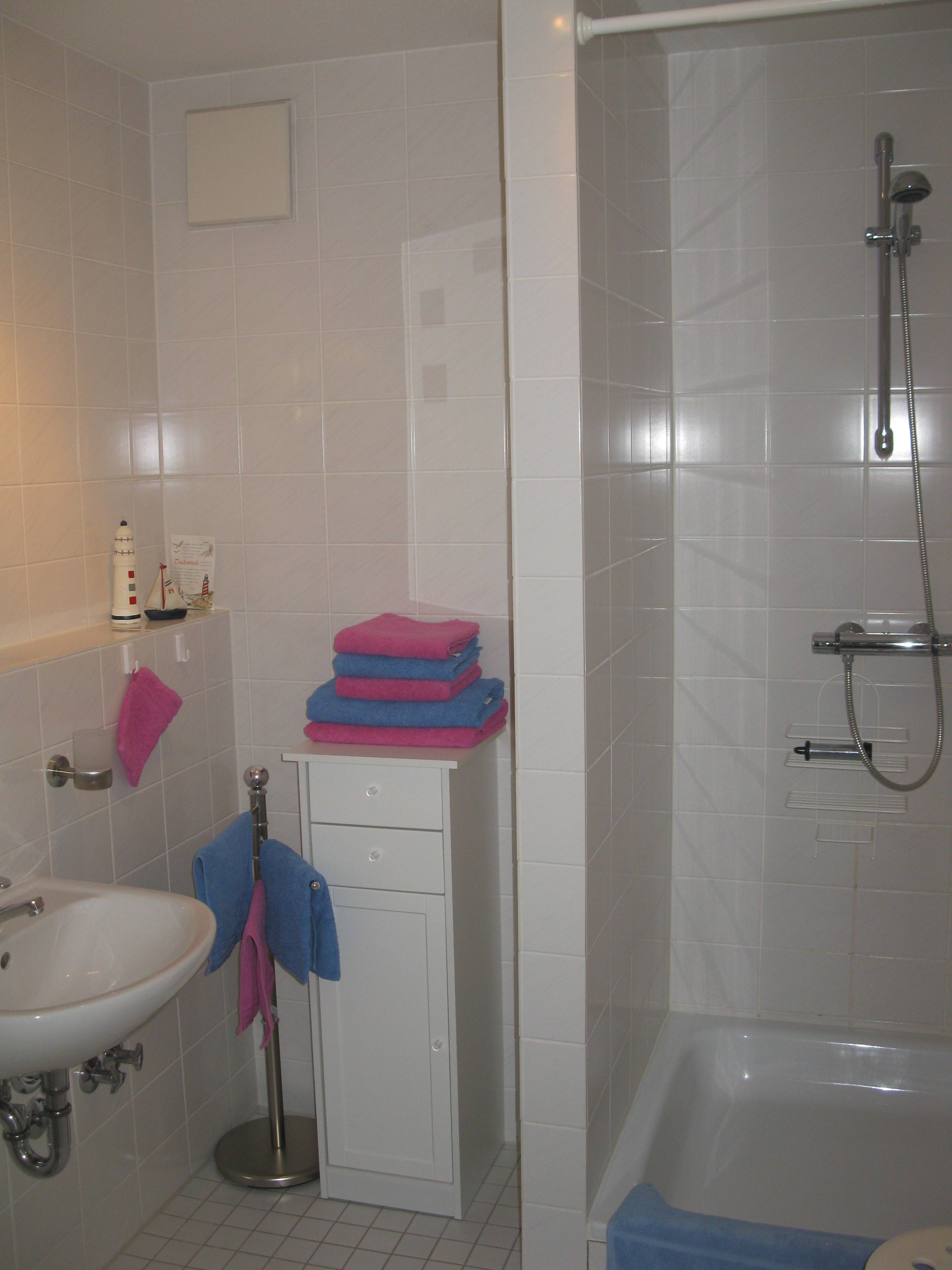 Ein Badezimmer mit Waschbecken, Spiegel, Handtuchhalter, einer Tür und einer Duschkabine.