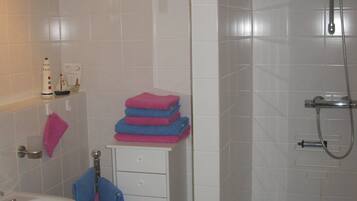 Ein Badezimmer mit Waschbecken, Spiegel, Handtuchhalter, einer Tür und einer Duschkabine.