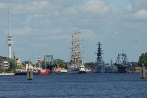 Ein Hafen mit verschiedenen Schiffen, darunter ein Segelschiff und ein modernes Marinefahrzeug.