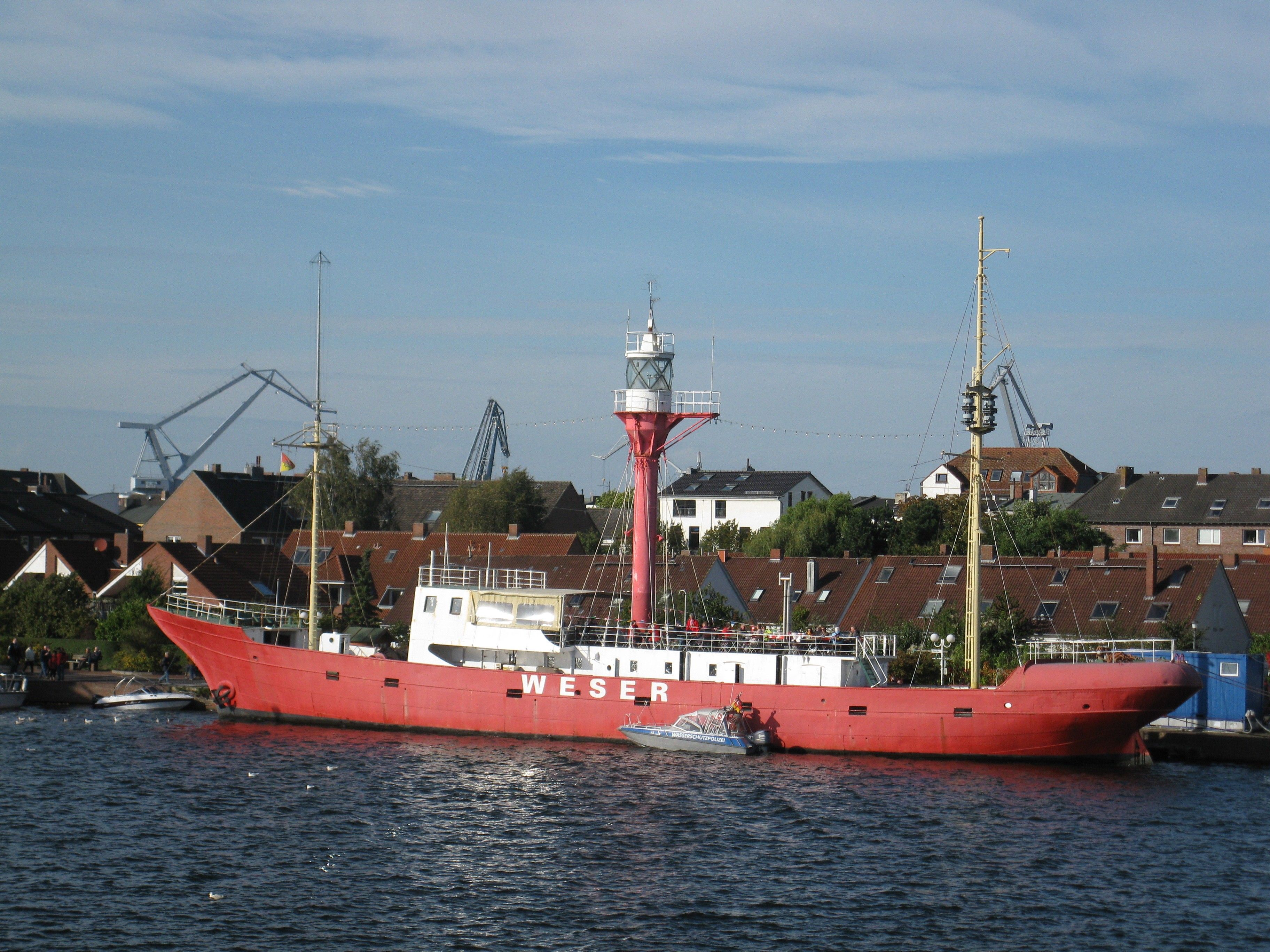 Un vaixell vermell gran amarrat al port, amb un far al fons.