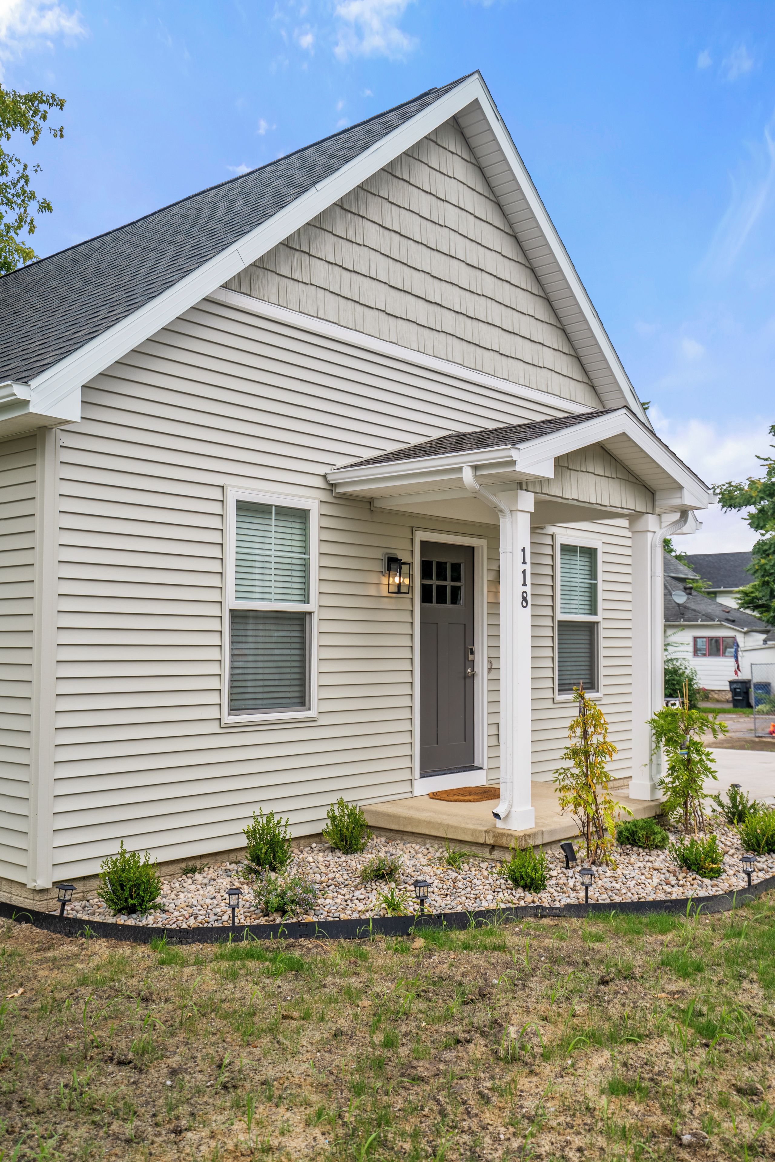 A single-story house with a gabled roof, a front porch, and a small front yard with a gravel pathway and young trees.