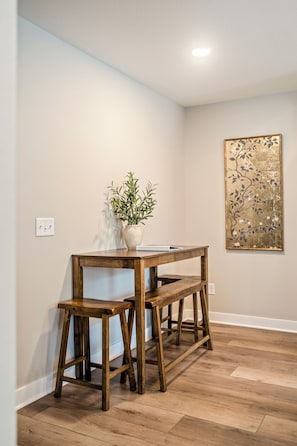Quarto com um banco de madeira, uma pequena mesa com uma planta e um quadro pendurado na parede.