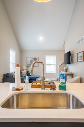A kitchen with a stainless steel sink, a faucet, and a countertop with a bottle of dish soap and a sponge.