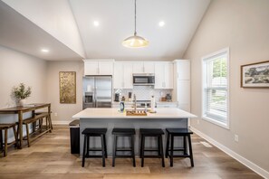 A modern kitchen with white cabinets, stainless steel appliances, a central island with bar stools, and a hanging pendant light.