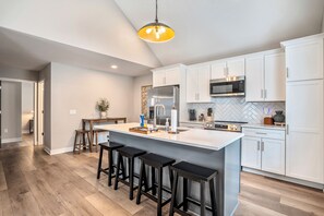 A modern kitchen with white cabinets, a central island with bar stools, stainless steel appliances, and a pendant light. - Stay close to your student in this private, brand-new home near campus and downtown Bowling Green, Ohio. Walkable to great dining, enjoy modern comfort, and relax in a peaceful, thoughtfully designed space. (Bowling Green)