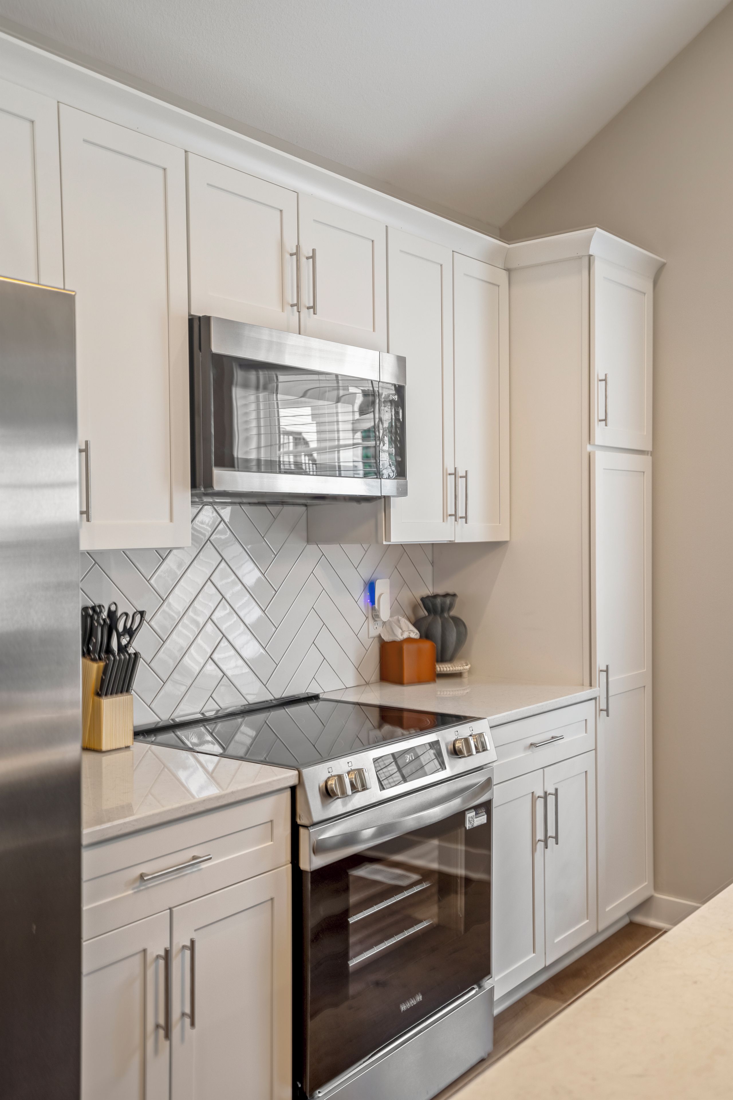 Una cocina moderna con armarios blancos, un refrigerador de acero inoxidable, un microondas y un horno.
