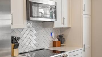 Una cocina moderna con armarios blancos, un refrigerador de acero inoxidable, un microondas y un horno.
