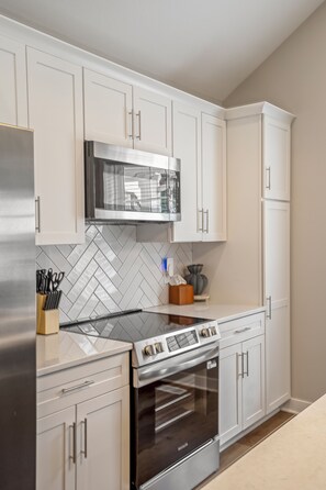 A modern kitchen with white cabinetry, a stainless steel refrigerator, a microwave, and an oven.