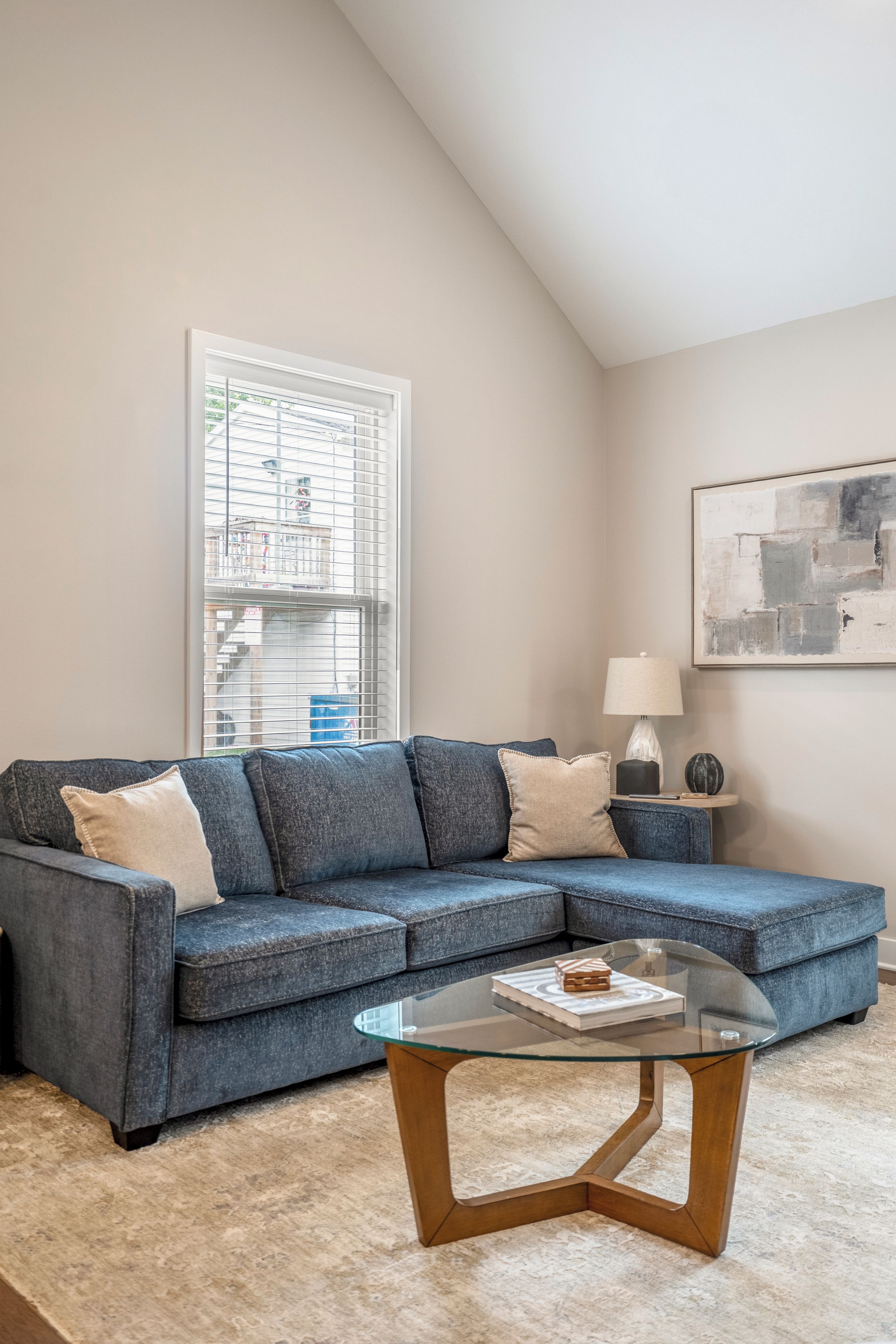 A living room with a sectional sofa, a glass coffee table, a lamp, and a painting on the wall.