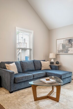 A living room with a sectional sofa, a glass coffee table, a lamp, and a painting on the wall.