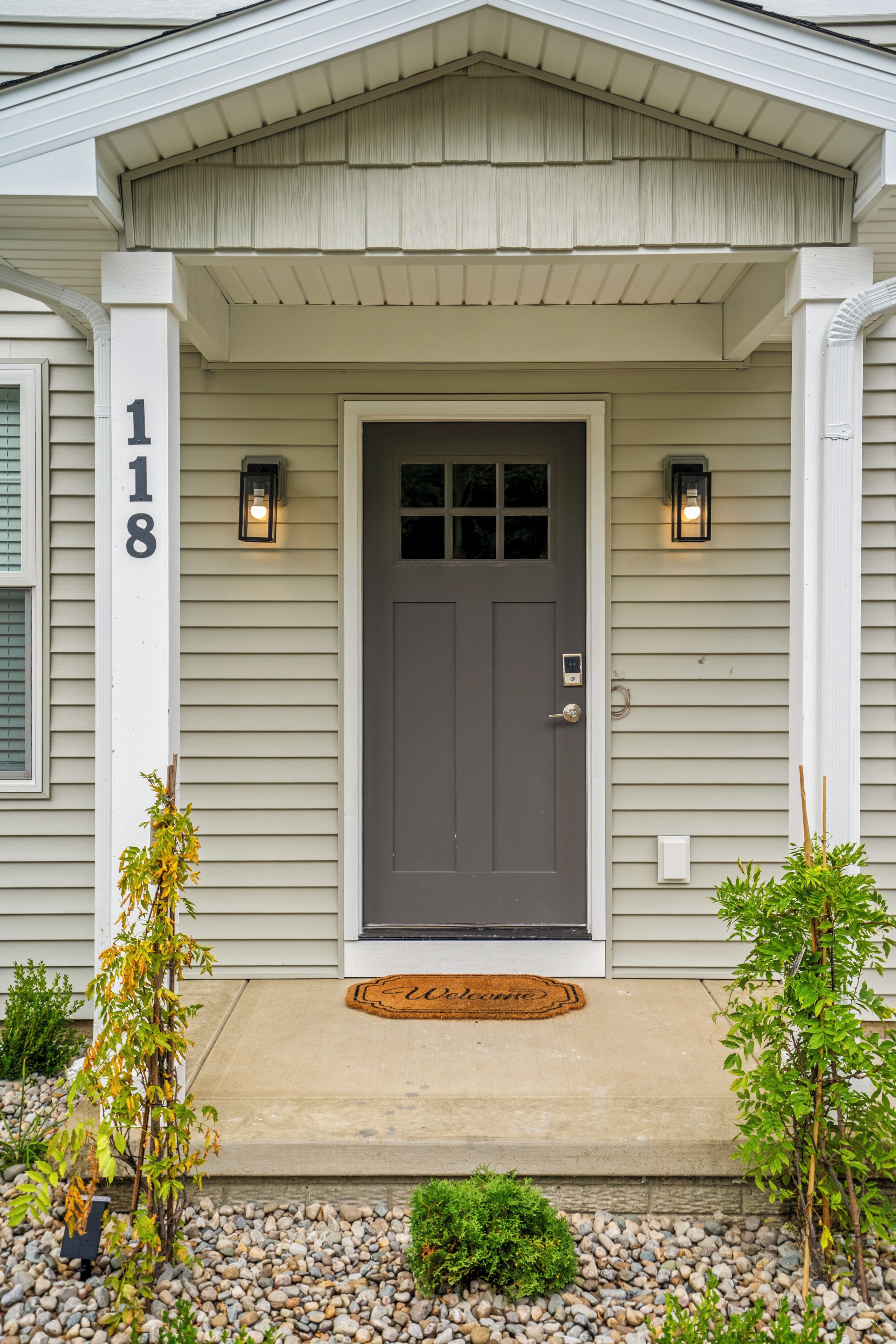 A house with a gray front door, a number '118' on the wall, and two wall-mounted lights.