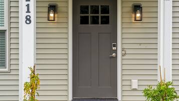 A house with a gray front door, a number '118' on the wall, and two wall-mounted lights.