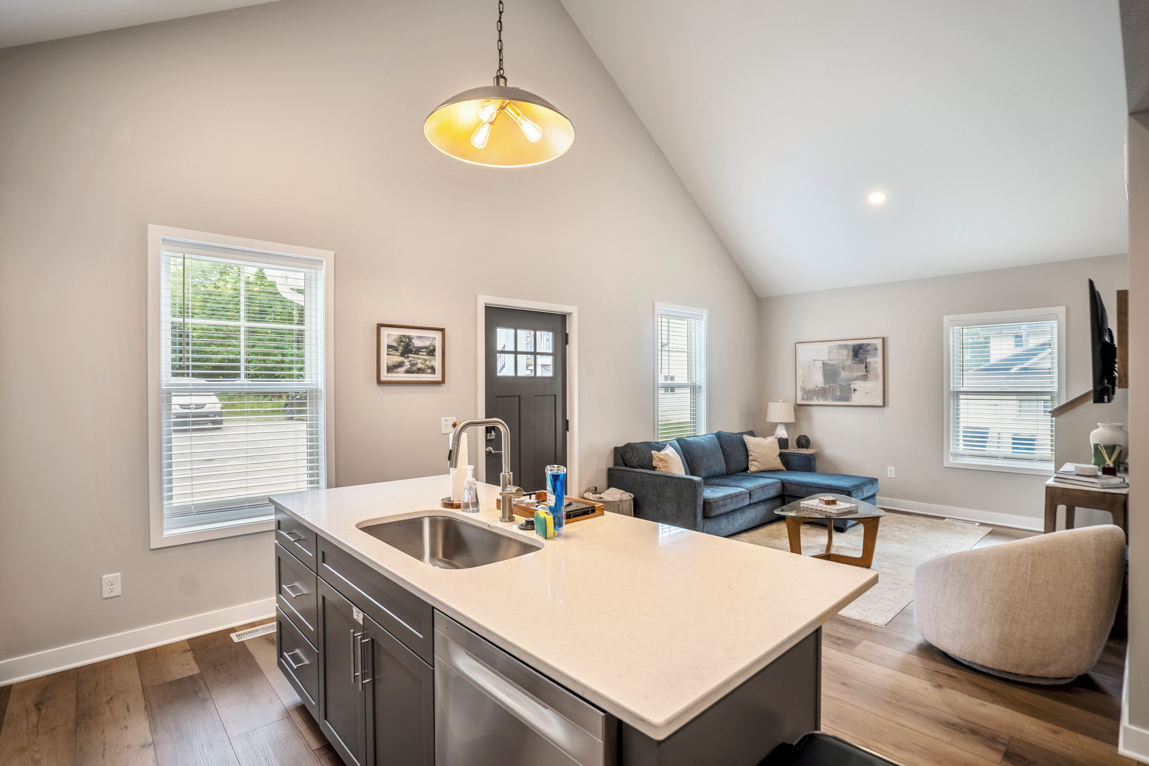 A modern kitchen with a large island, a dining area with a blue sofa, and a living room with a grey sofa.