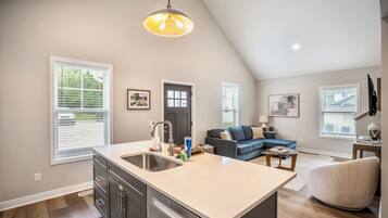 A modern kitchen with a large island, a dining area with a blue sofa, and a living room with a grey sofa.