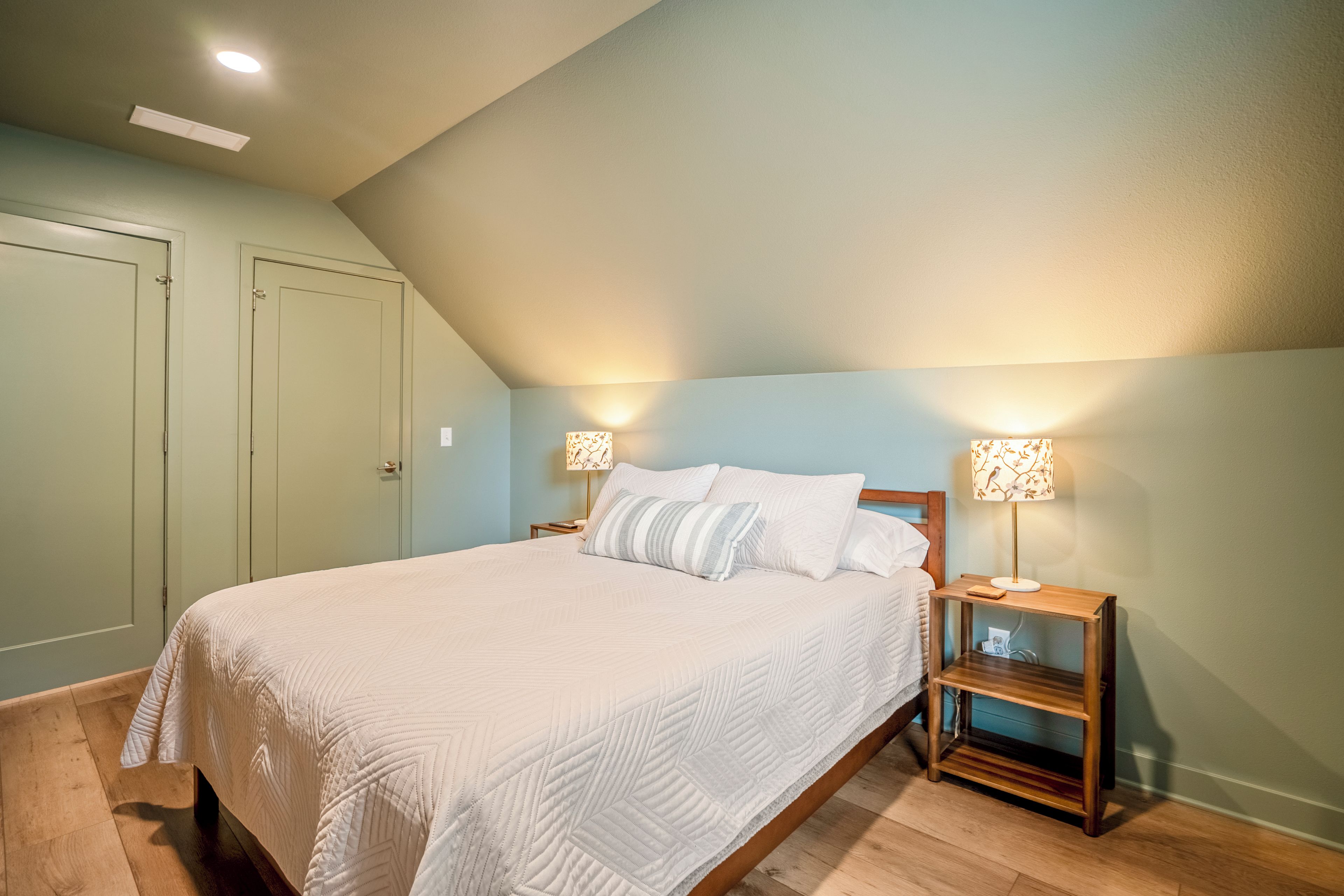 Een slaapkamer met een eenpersoonsbed, twee nachtkastjes met lampen, en een deur.