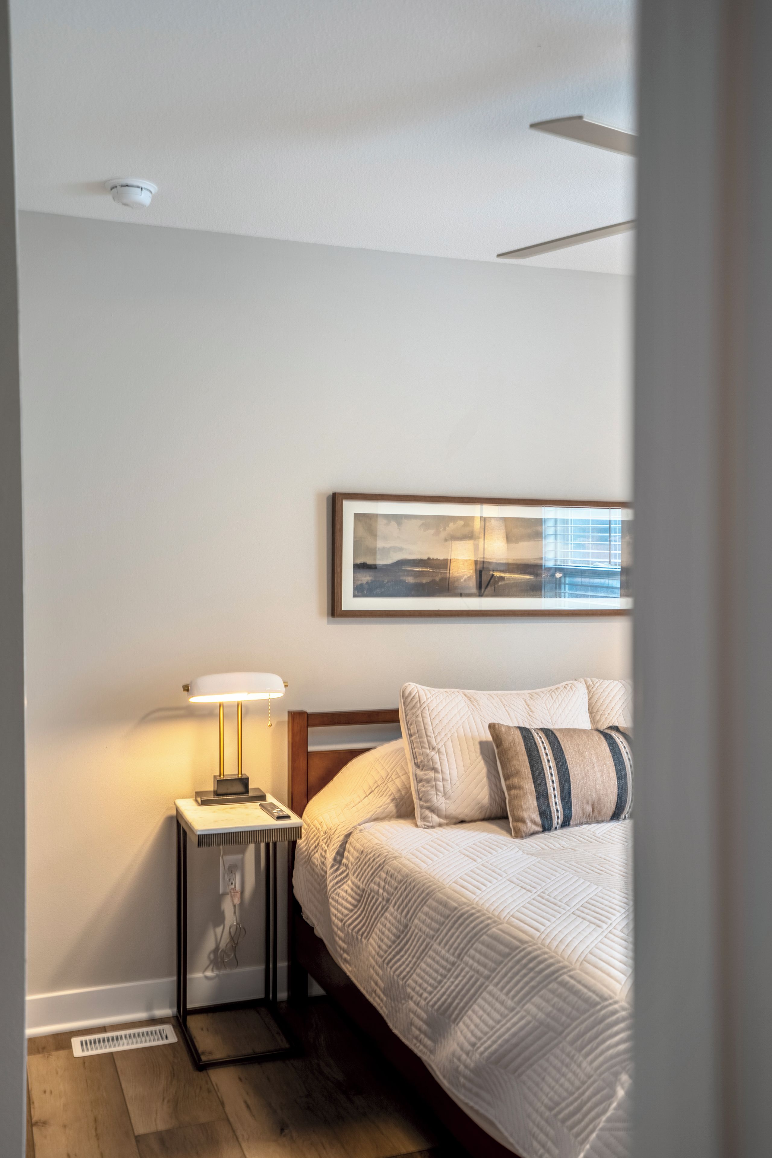 Una camera da letto con un letto, un comodino con una lampada, un quadro appeso al muro e una finestra.