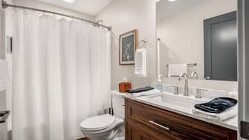 A bathroom with a shower curtain, toilet, sink with a marble countertop, wooden vanity, and a large mirror.
