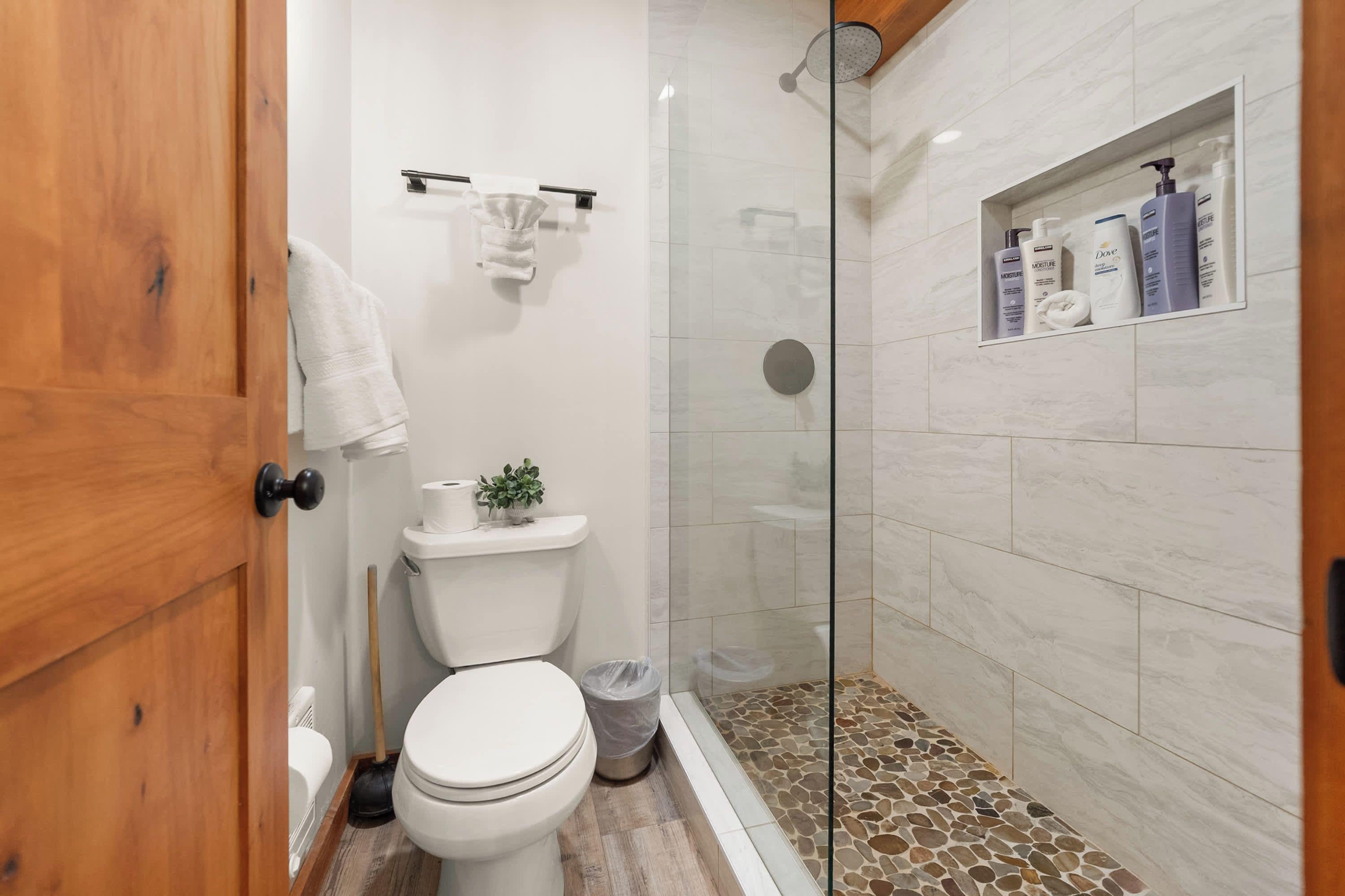 A bathroom with a toilet, a shower enclosure, and a shelf with toiletries.