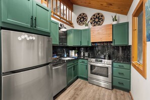 A kitchen with green cabinets, a stainless steel refrigerator, a stove, and a microwave. - Petros Place Ptarmigan Village Hot Tub Pool (Whitefish)
