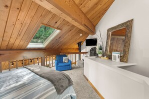 Ein Schlafzimmer mit schrägem Dach, einem Bett, einem blauen Sessel und einem kleinen Schreibtisch mit Spiegel.