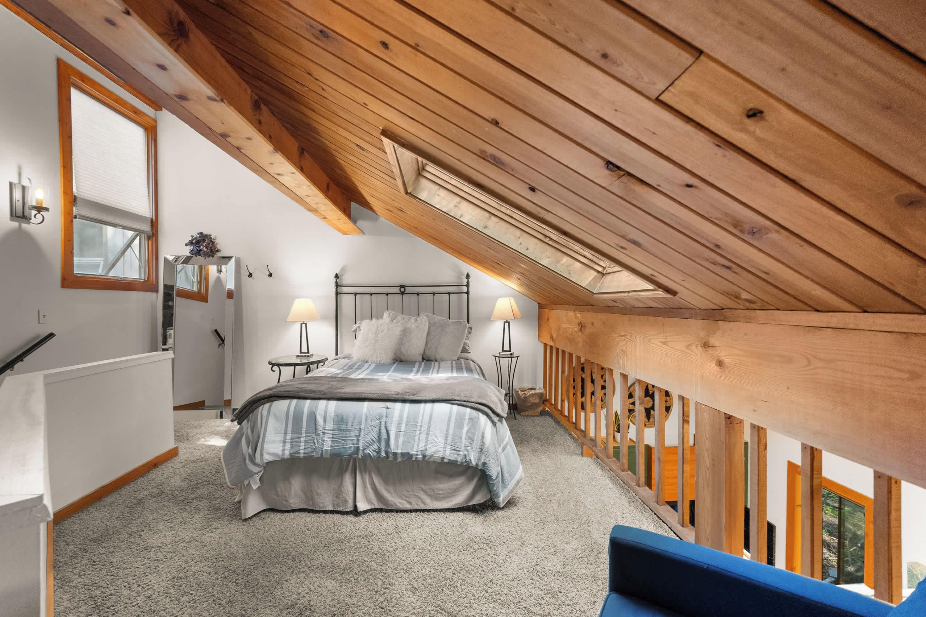 Una camera da letto con soffitto spiovente, un letto con copriletto a righe, due abat-jour e una ringhiera in legno.