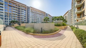 Un edifici residencial modern amb diversos pisos, un pati paisatjat amb palmeres i un camí amb rajoles.