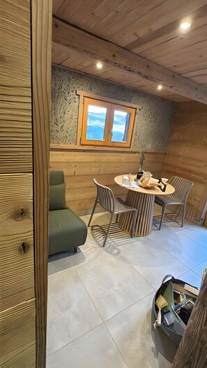 Una habitación acogedora con techo de madera, ventana con vistas, una mesa redonda con sillas y un sofá verde.