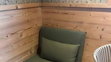 Eenpersoonskamer met een wand van houten panelen, een met groen bekleden bed en een gestreepte stoel.