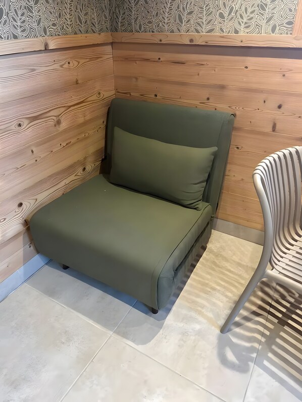 Quarto individual com parede de painel de madeira, cama estofada verde e cadeira listrada.