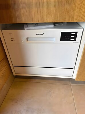 Máquina de café compacta e branca, com painel de controle e uma alça, sobre um armário de madeira.