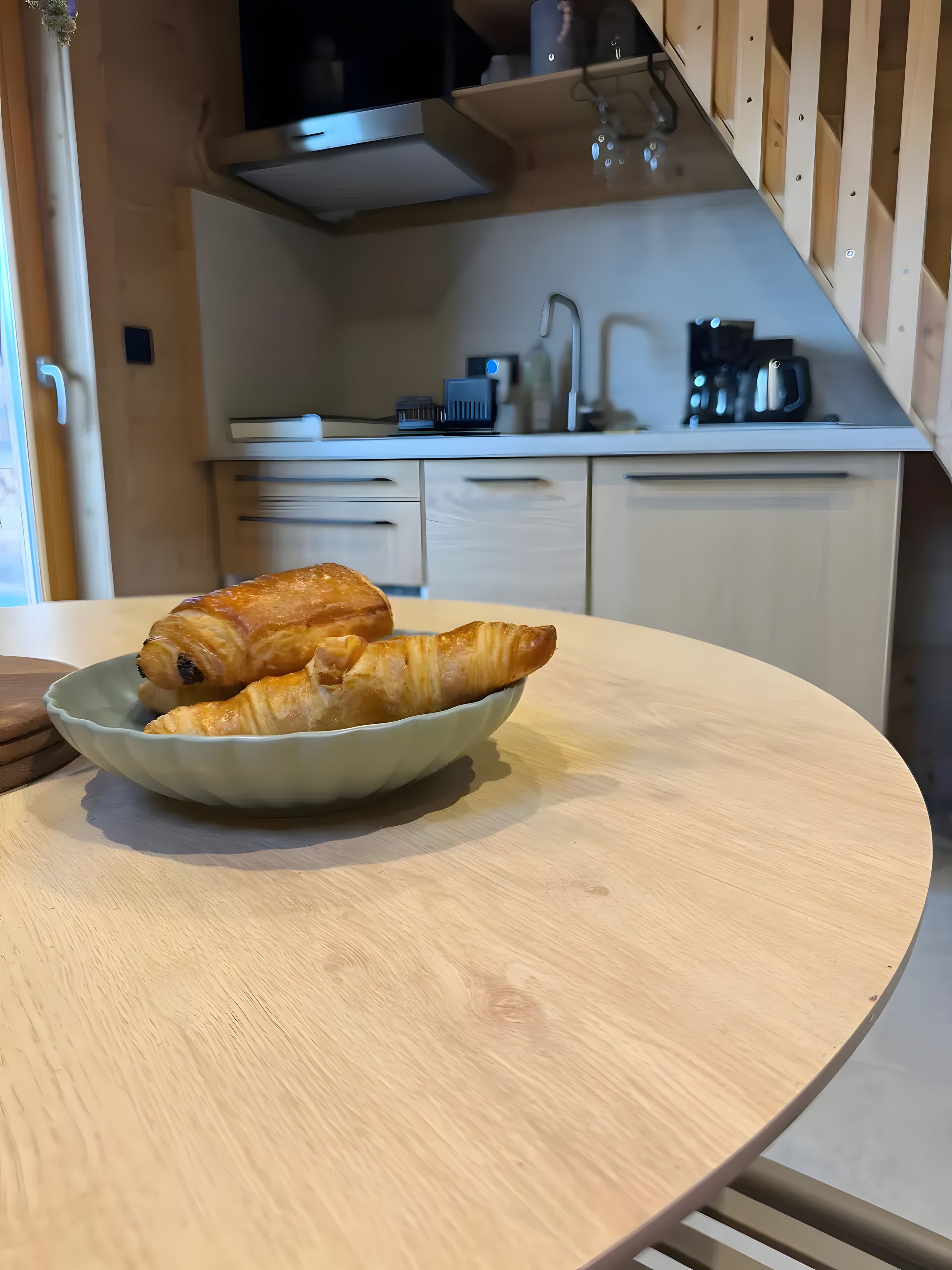 Keittiössä on pyöreä pöytä, kulho täynnä croissantteja ja kahvinkeitin.