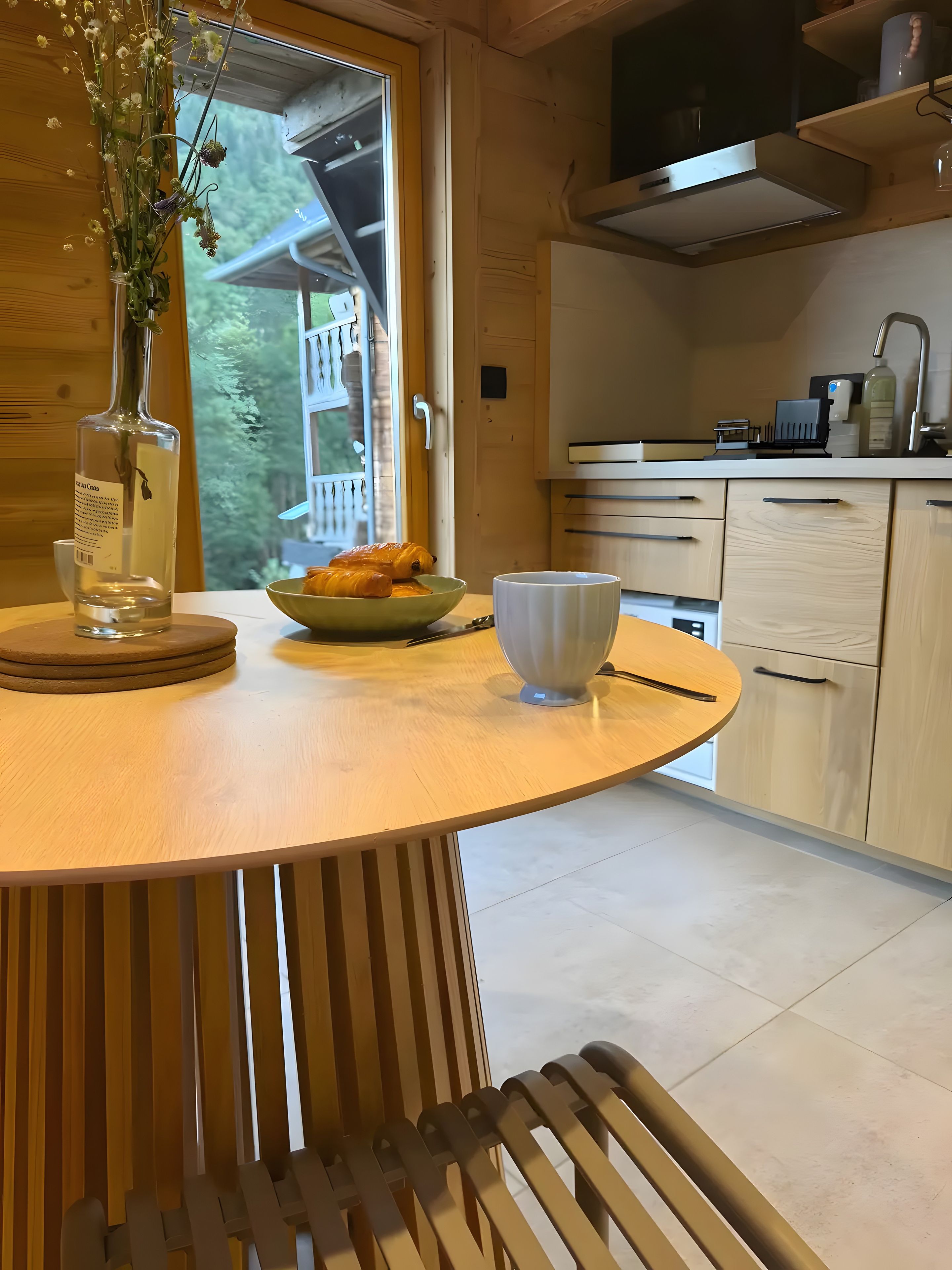 A wooden dining table with a vase of flowers, a bowl of croissants, and a white mug.