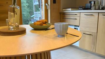 A wooden dining table with a vase of flowers, a bowl of croissants, and a white mug.