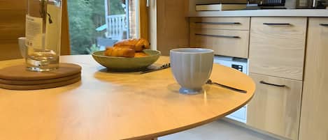 A wooden dining table with a vase of flowers, a bowl of croissants, and a white mug.