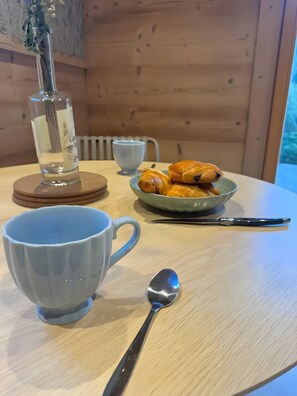 Interior de madeira com uma mesa posta para o café da manhã, incluindo croissants, uma xícara, uma colher e uma garrafa.