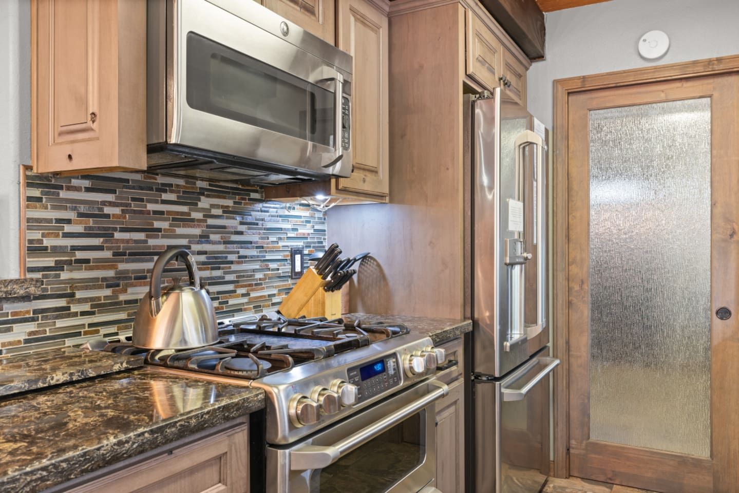 A kitchen with a stainless steel stove, microwave, and refrigerator, a tiled backsplash, and wooden cabinets.